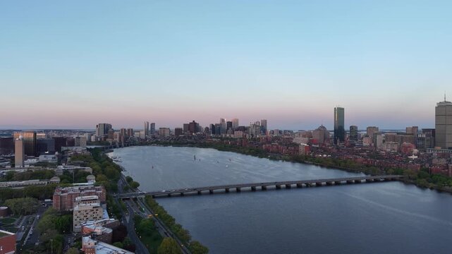 Golden hour aerial drone view of the Boston skyline, featuring the Prudential and John Hancock towers rising above the historic Back Bay neighborhood and the calm waters of the Charles River.