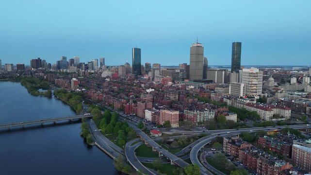 Golden hour aerial drone view of the Boston skyline, featuring the Prudential and John Hancock towers rising above the historic Back Bay neighborhood and the calm waters of the Charles River.