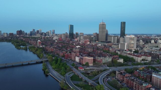 Golden hour aerial drone view of the Boston skyline, featuring the Prudential and John Hancock towers rising above the historic Back Bay neighborhood and the calm waters of the Charles River.