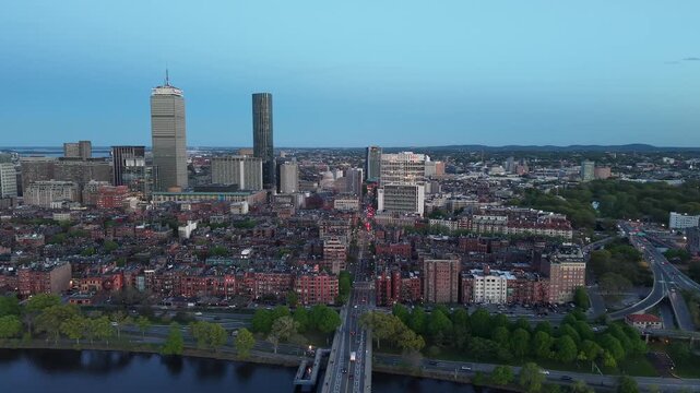 Golden hour aerial drone view of the Boston skyline, featuring the Prudential and John Hancock towers rising above the historic Back Bay neighborhood and the calm waters of the Charles River.