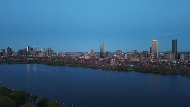 Golden hour aerial drone view of the Boston skyline, featuring the Prudential and John Hancock towers rising above the historic Back Bay neighborhood and the calm waters of the Charles River.