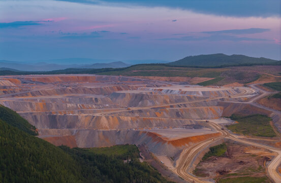 Expansive open pit mine at sunset with layers of earth and surrounding hills with ore