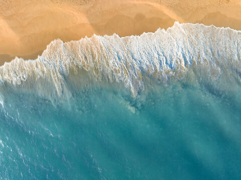 Blue ocean water meeting sandy beach coastline in aerial view. Natural seaside background with copy space perfect for tourism campaigns, summer marketing visuals, and coastal lifestyle concepts.