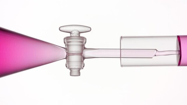 Extreme close of clear pink fluid flowing from separatory funnel through the glass stopcock into a test tube, filling it up on neutral white surface | Lychee liquid extract cosmetic mixture concept