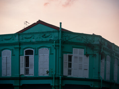 Vintage green building facade with white shutters under pink sky