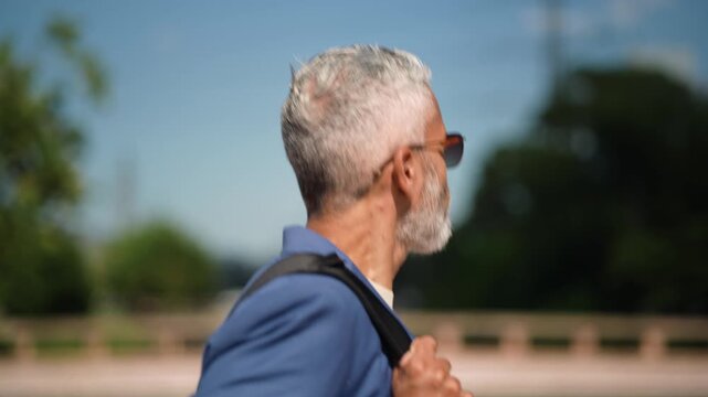 Close up profile of mature Brazilian businessman with glasses and backpack walking on urban sidewalk commuting in city