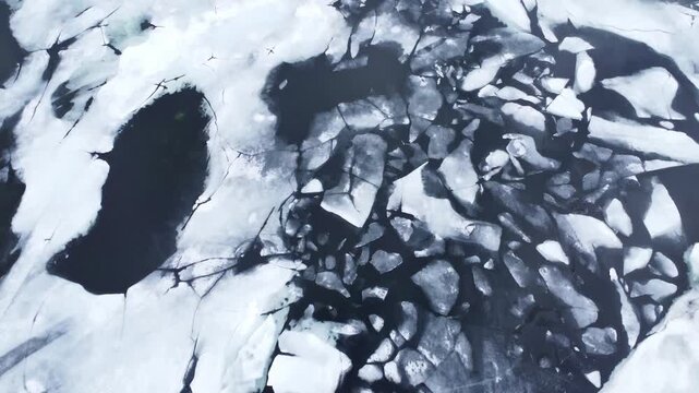 Aerial view of cracked ice floes and melting snow patterns on the dark waters of Hardangervidda plateau in Ullensvang, Vestland, Norway.