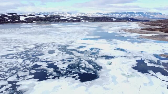 Aerial view of the melting ice on Hardangervidda plateau with rocky shores and distant mountains in Ullensvang, Vestland, Norway.