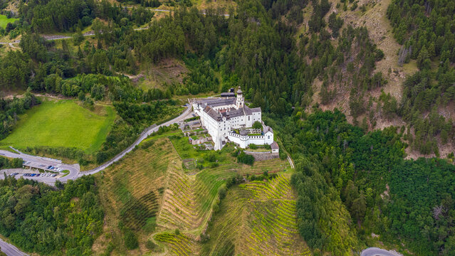 4K aerial view of Marienberg Abbey, Europe's highest Benedictine monastery in South Tyrol, Italy. Scenic white baroque basilica surrounded by alpine mountains and lush green vineyards in summer.