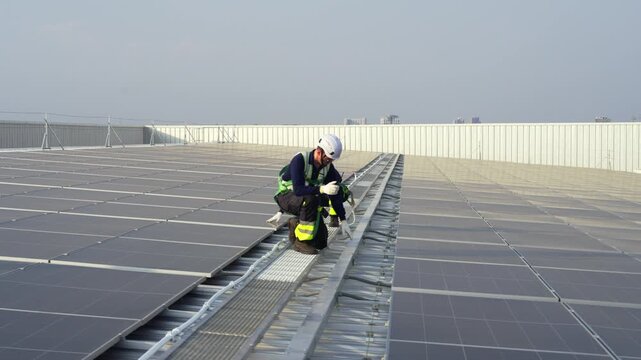 Engineers maintenance solar panels rooftop green energy technician safety inspection on building with harness and helmet, crew adjusts mounting rail, tightens mounts along metal walkway under sky