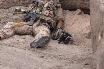 Fototapeta premium Soldier rests on ground with weapon and gear in conflict area