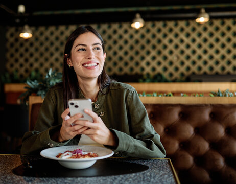Young woman enjoying eating lunch and using a mobile phone at restaurant