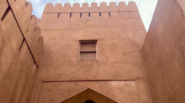 Historic Nizwa Fort after rain under clear blue sky with Omani flag and mosque minaret in background. Nizwa, Oman - May 14 2026