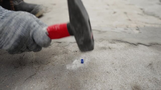 Worker Hammering Plastic Dowel into Concrete