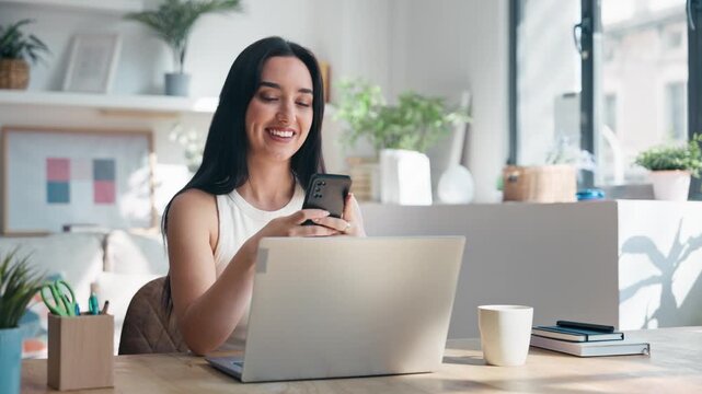 Video of beautiful woman using smartphone while working with laptop in the livingroom at home