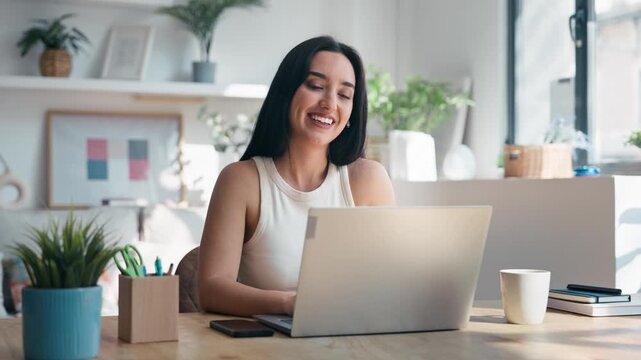 Video of smiling woman doing a videocall with laptop in the livingroom at home