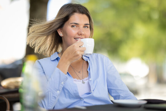 Woman enjoys coffee at a caf while sitting at a table under a tree on a sunny day
