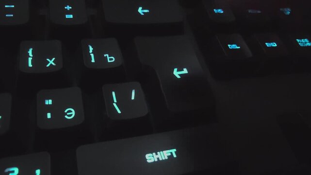 Close-up view of illuminated keyboard showing fingers pressing keys, highlighting the action of typing with visible symbols and letters on the keys in a dark environment