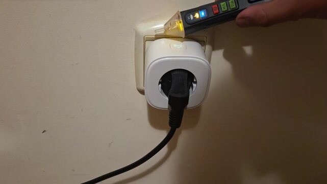 Handheld tracking close up of hand testing electrical outlet with voltage tester on indoor wall