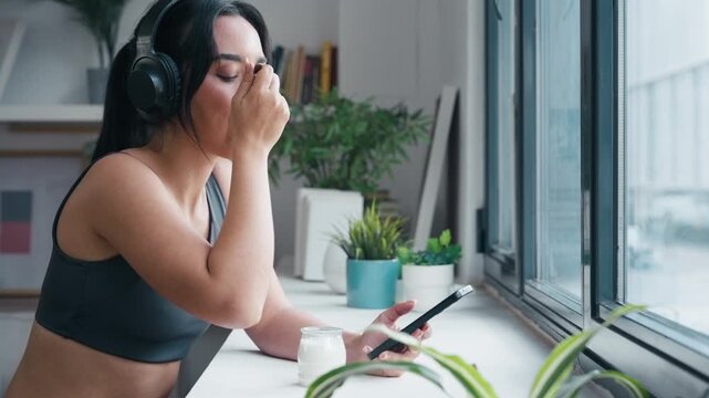 Video of f sporty woman eating yogurt while listening to music with headphones at home