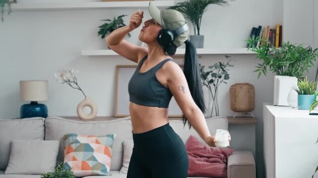 Video of sporty woman eating yogurt while dancing and listening to music with headphones at home