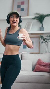 Video of sporty woman eating yogurt while dancing and listening to music with headphones at home