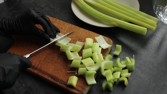 Hands in black gloves slice fresh celery on a wooden cutting board for preparation, showcasing a healthy lifestyle.