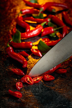 Kitchen knife and ​​​​wedges of red hot chili peppers on a kitchen table.