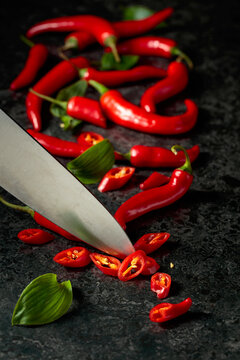 Kitchen knife and ​​​​wedges of red hot chili peppers on a kitchen table.
