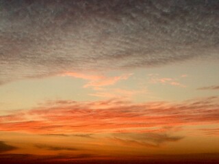 Fototapeta premium Warm sunrise sky with soft orange and pink clouds layered above the horizon.