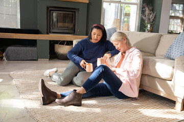 Fototapeta premium Two women sitting on rug with mugs pointing at paper causing animated decor swatches changing sofa