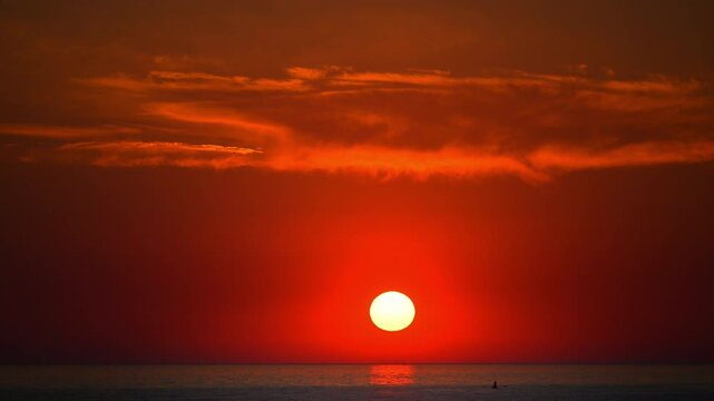Stunning red sunset over calm sea with glowing sun and dramatic clouds, cinematic 4K slow motion.