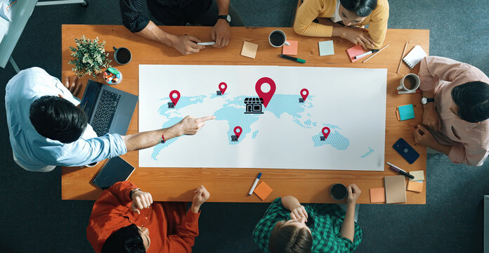 Diverse team members gather in an office setting to discuss business strategies using a digital map with location pins, highlighting ideas for global expansion and collaboration. Gantry