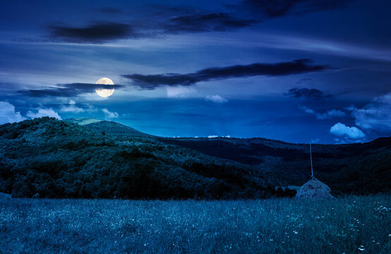 rural fields near pikui mountain in summertime at night. full moon over beautiful view of agricultural area. gorgeous mountain ridge with haystack on a grassy pasture. mysterious summer scenery