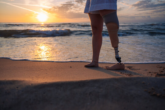 Woman with prosthetic leg standing on beach at sunset