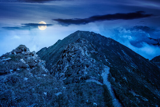 mountain scenery in summer at night. gorgeous mountainous landscape. background with rocky cliffs and grassy hillsides under a cloudy sky. full moon over ridge of mysterious mountains