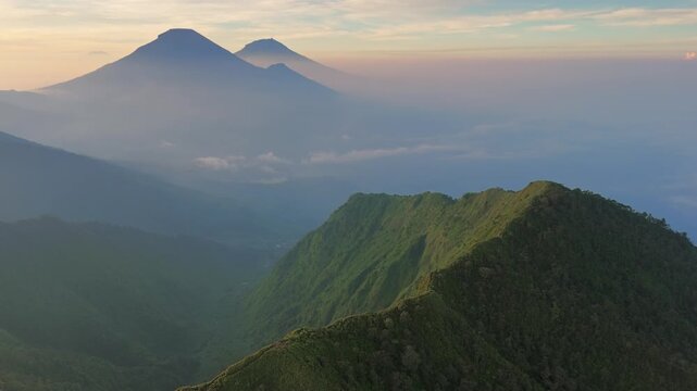 Aerial view of the Dieng Plateau featuring lush green mountain ridges and volcanic peaks shrouded in morning mist Kejajar, Central Java, Indonesia.