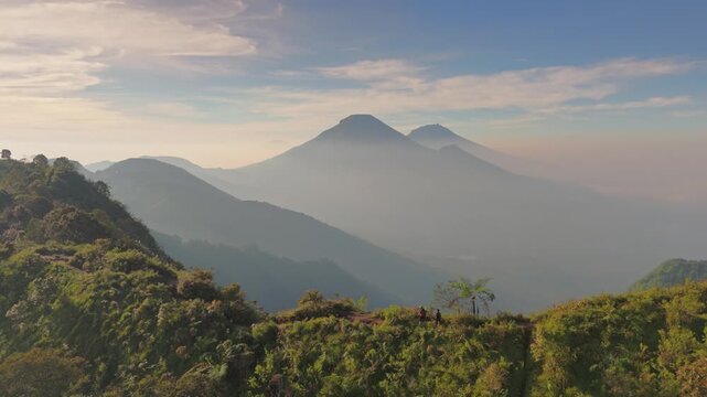 Aerial view of Dieng plateau with misty volcanic peaks and lush green mountain ridges under a soft sky in Kejajar, Central Java, Indonesia.