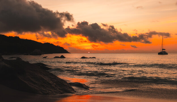 Anse Lazio beach view, calm ocean water with soft waves is under red sunset sky. Coastal landscape with silhouettes of rocks. Praslin island, Seychelles