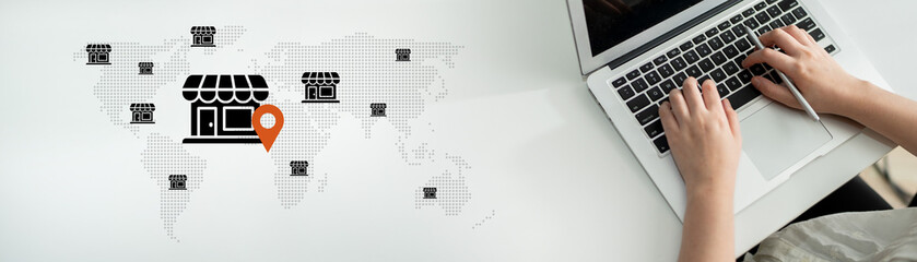 A person is using a laptop while surrounded by a world map and store icons, illustrating the...