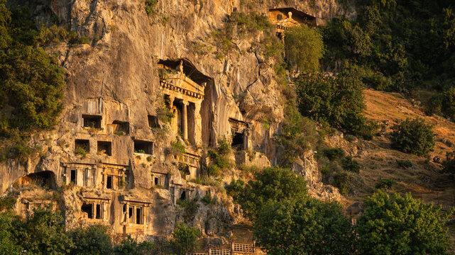 Ancient Lycian rock tombs carved into the mountain cliff in Fethiye, Turkey at golden hour.