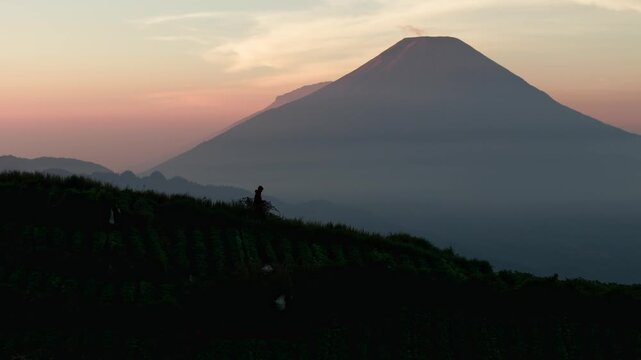Aerial view of a person standing on a ridge overlooking a majestic volcano during a vibrant sunrise in Dieng, Kejajar, Central Java, Indonesia.
