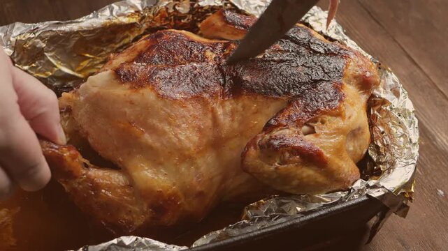 A woman's hands use a knife to cut a whole roast turkey with its crust on foil. Medium shot.