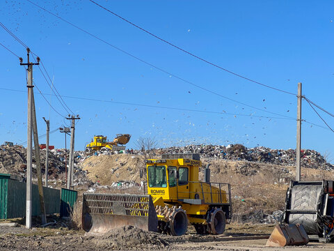 Lutsk, Ukraine &ndash; March 14, 2026: Heavy machinery operates at a municipal landfill, sorting and managing waste while seagulls fly around in the background on a sunny day