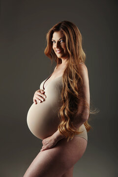 Beautiful pregnant model profile portrait with long wavy healthy hair isolated on grey studio background. Tummy. Pregnancy.