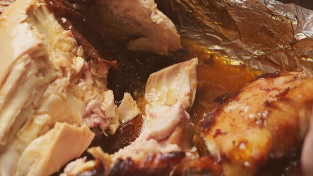 A woman's hands use a knife to cut a whole chicken baked with a spice crust on foil. Medium shot.