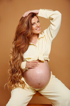 Pregnancy. Smiling pregnant woman touchin tummy isoalted on yellow studio background. Beautiful woman with long wavy hair happy and enjoy with her belly.