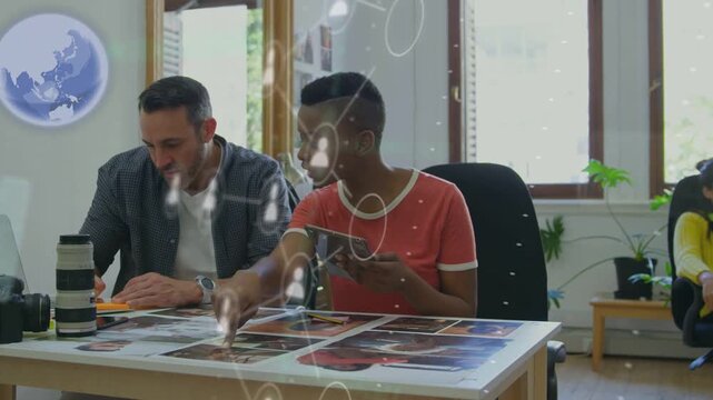 Woman in red tapping tablet and guiding design review, man noting edits, UI overlay showing assets