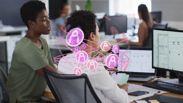 Seated woman holding notes, peer leaning and pointing, pink holo emerging, guiding tech on screens