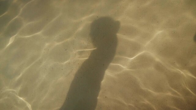 Human shadow silhouette dancing on the sandy sea bottom
